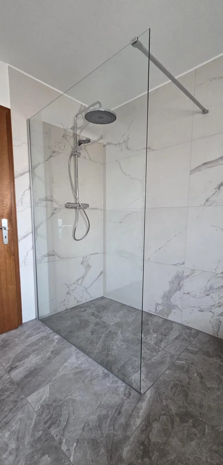 Geflieste Dusche mit Glasabtrennung und grauem Boden
