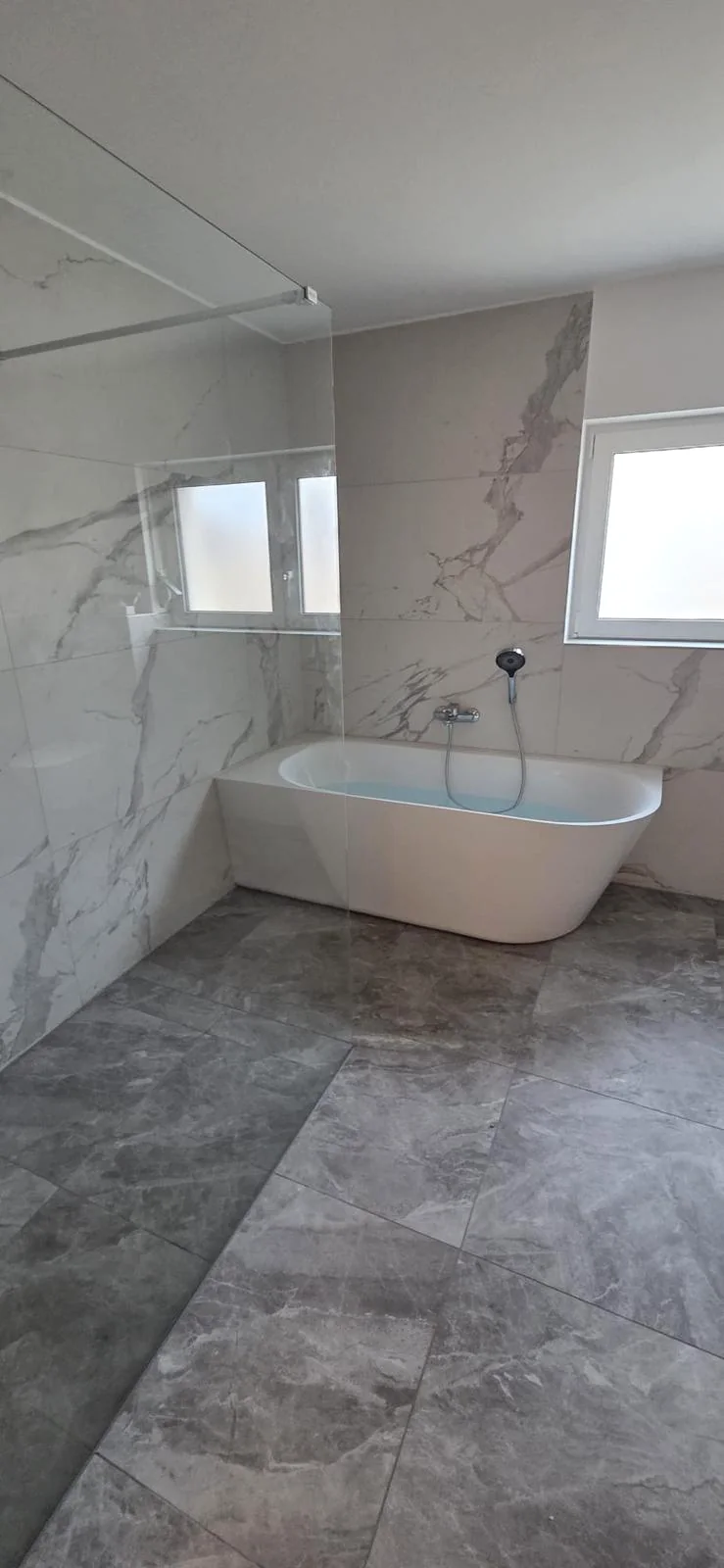 Helles Badezimmer mit Badewanne und großformatigen Wandfliesen