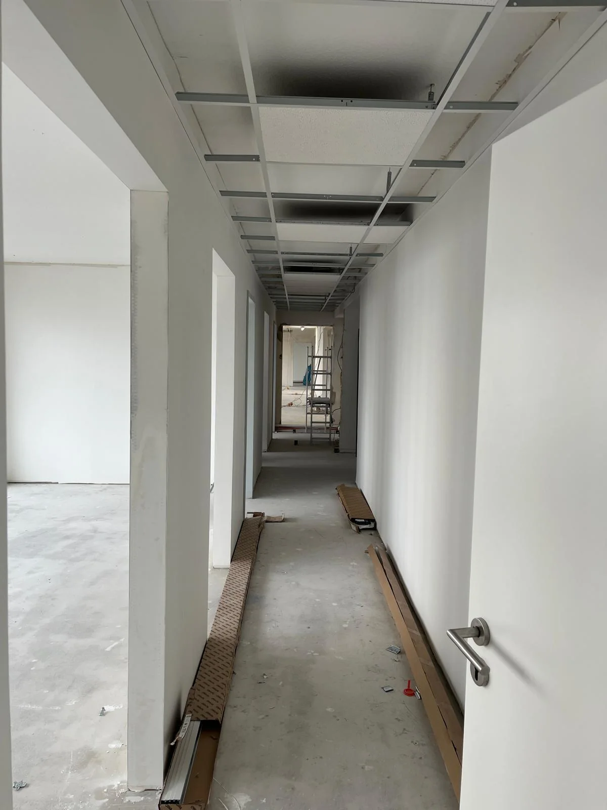 Flur mit unbelegtem Boden und offener Rasterdecke