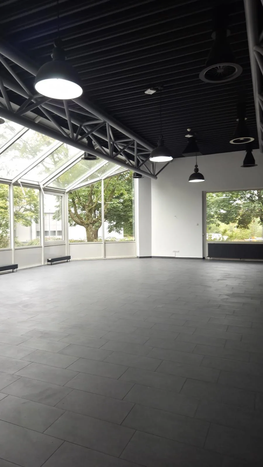 Halle mit Glasfront, Pendelleuchten und grauen Bodenfliesen