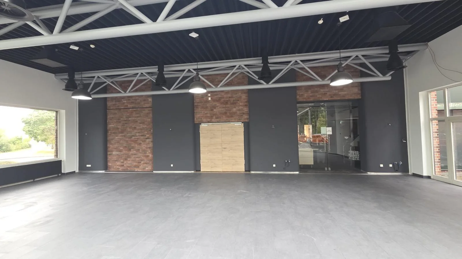 Halle mit Ziegelwand, dunkler Decke und grauem Fliesenboden