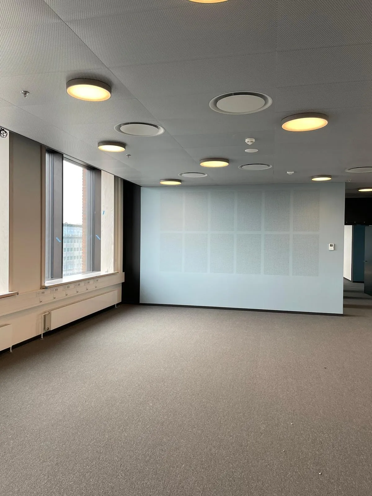 Helle Akustikwand in einer Bürofläche mit Fensterband und runden Deckenleuchten