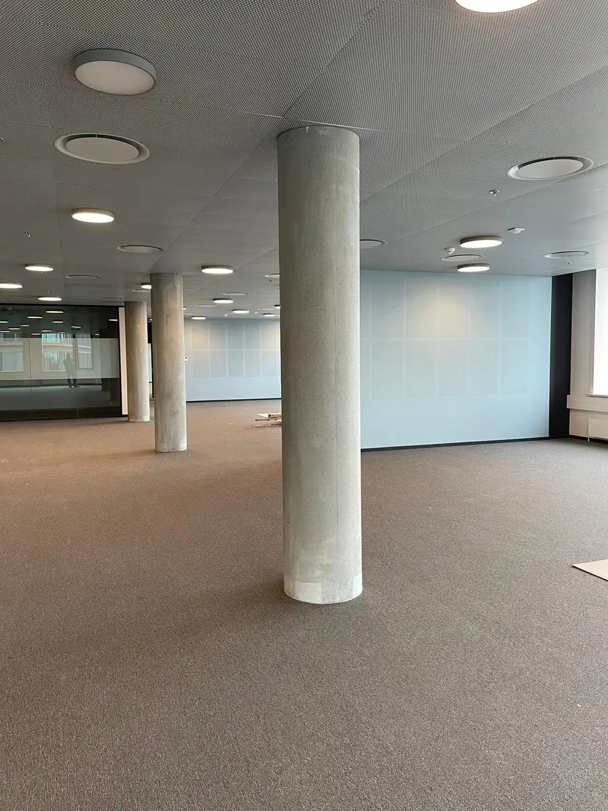 Offene Bürofläche mit akustischen Trennwänden, runden Deckenleuchten und Säulen