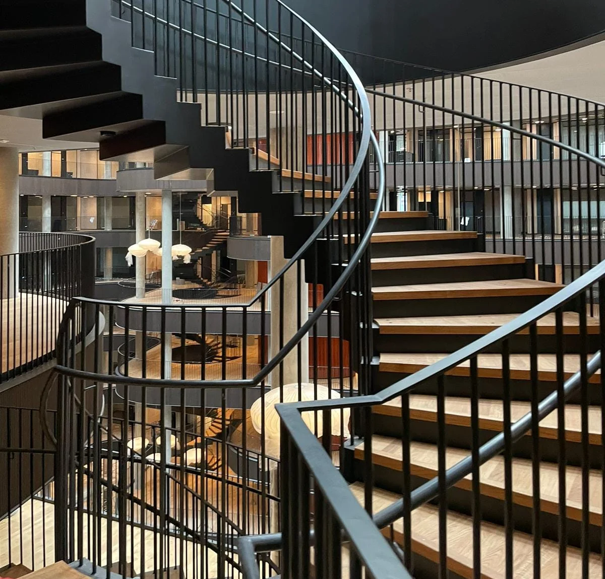 Geschwungene Treppe mit dunklem Geländer und Holzstufen in einem hellen Atrium