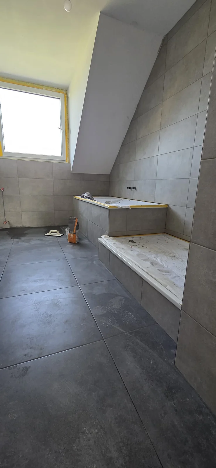 Dachgeschossbad während der Fliesenarbeiten mit grau gefliester Badewannenverkleidung