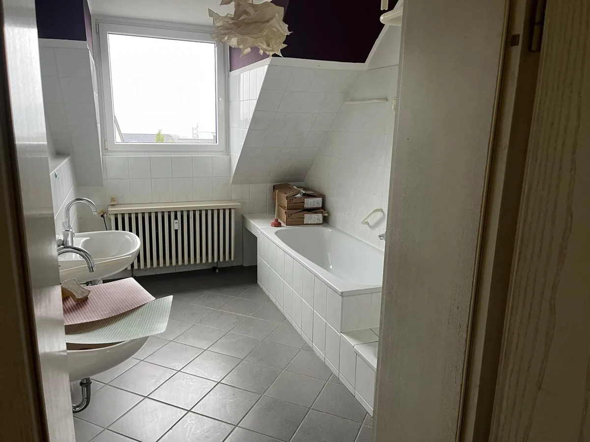 Badezimmer unter der Dachschräge mit weißer Badewanne und alten Bodenfliesen