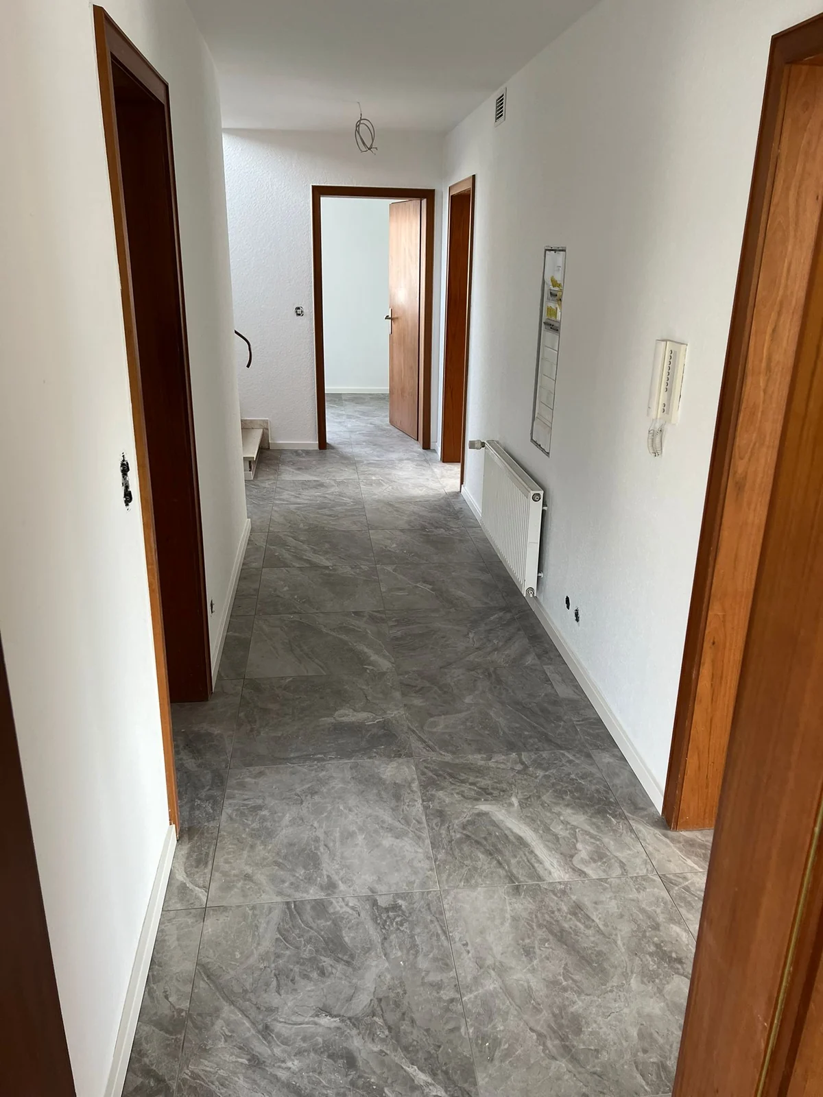 Flur mit grauem Bodenbelag, weißen Wänden und Holztüren