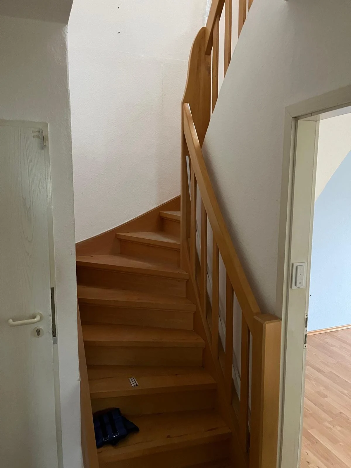Gewendelte Holztreppe mit Holzhandlauf zwischen hellen Innenwänden